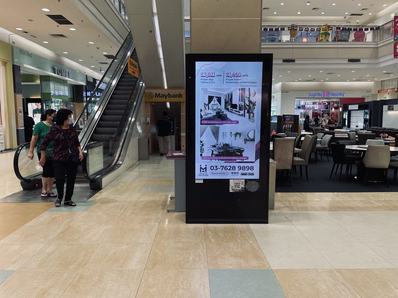 Kesion Malaysia digital standing screen displaying a PR1MA housing advertisement near a Maybank branch.