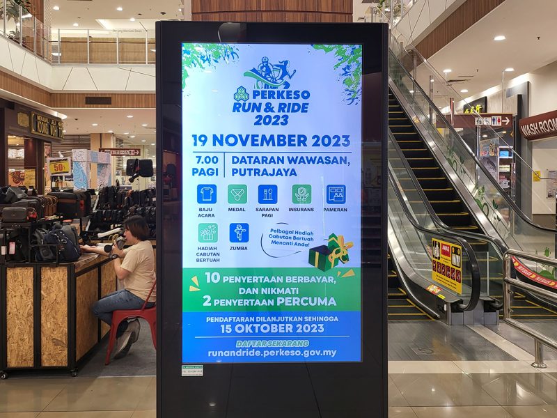 Kesion Malaysia digital standing screen advertising the PERKESO Run & Ride 2023 event in a shopping mall.
