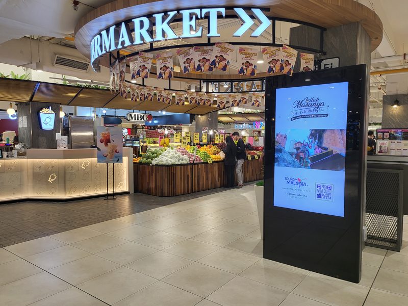 Kesion Malaysia digital standing screen showing a Tourism Malaysia advertisement for family holidays in front of a supermarket.