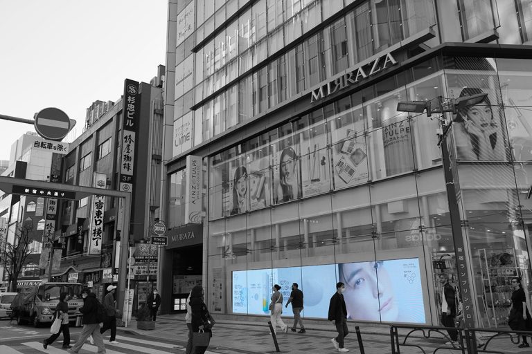 Black-and-white street photo of an Ainz & Tulpe storefront digital screen displaying a beauty advertisement in Tokyo
