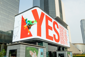 Massive wrap-around corner digital billboard displaying a 3D anamorphic tree frog and 'YES' typography campaign in Gangnam, Seoul.