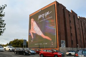 Massive digital billboard on a red brick warehouse displaying a Nasty Gal fashion campaign featuring Cara Delevingne.