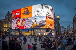 Massive curved digital billboard at Piccadilly Circus in London displaying multiple simultaneous advertisements, including Coca-Cola, Samsung, and Hyundai.
