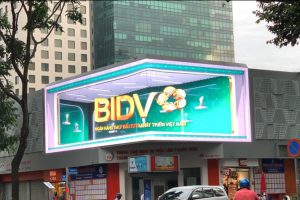 Massive 3D corner digital billboard displaying an anamorphic BIDV bank advertisement above the Youth Employment Service Center in District 1, Ho Chi Minh City.