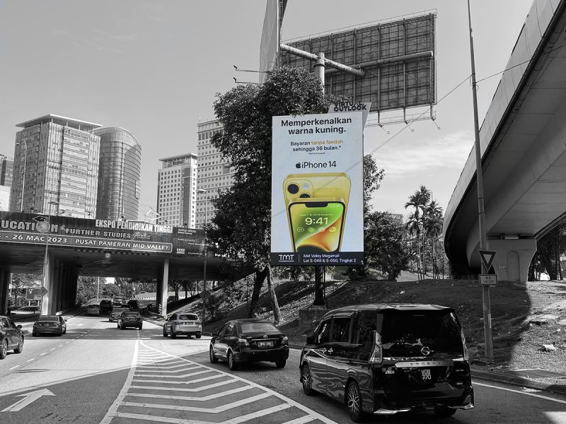 Outdoor digital billboard displaying a yellow iPhone 14 advertisement by TMT near Mid Valley by Kesion Malaysia