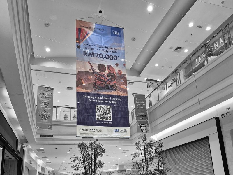 Large vertical hanging banner in AEON Mall promoting IJM Land's Seremban 2 Sutera 2-storey link homes with a holiday worth RM20,000